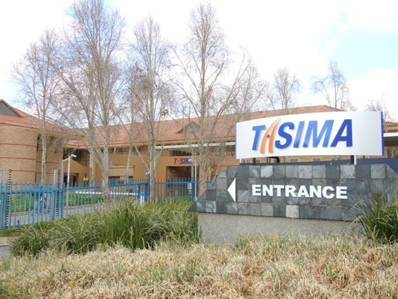 Front exterior view of the commercial property featuring a prominent entrance sign, brick facade, and secure perimeter fencing.