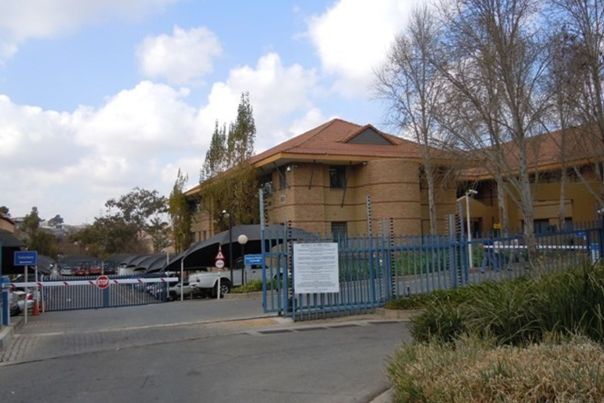 Front view of a commercial office building featuring face brick construction, tiled roofing, secure gated access, and covered parking facilities.