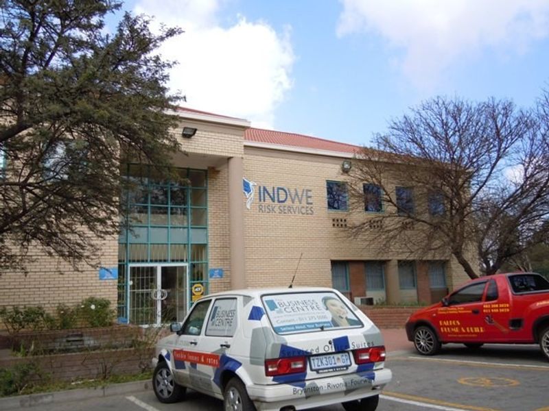 Front elevation of a commercial office building featuring a brick facade, tiled roof, and glass entrance area with signage.