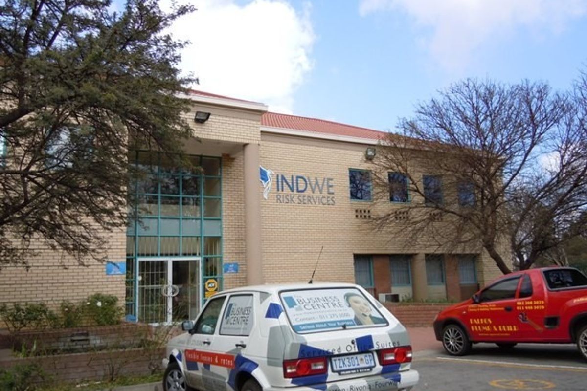 Front elevation of a commercial office building featuring a brick facade, tiled roof, and glass entrance area with signage.