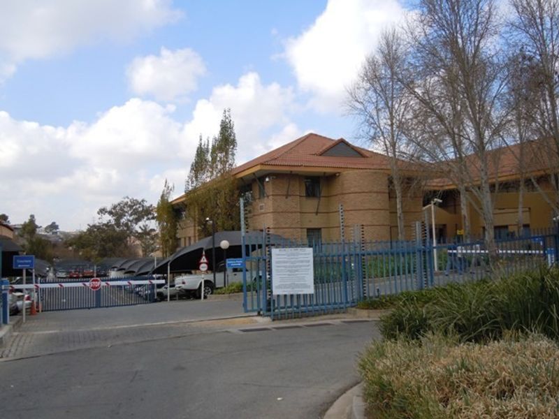 Front view of a commercial office building featuring face brick construction, tiled roofing, secure gated access, and covered parking facilities.