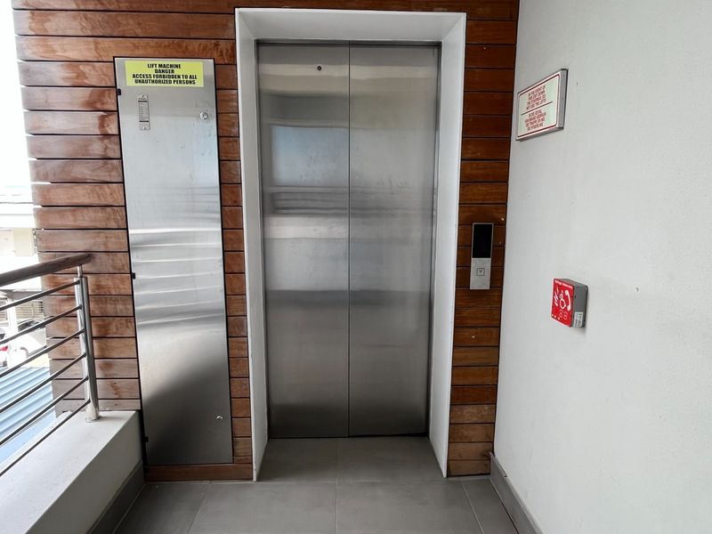A clean and well-maintained elevator lobby featuring stainless steel doors, timber slat wall paneling, and essential safety signage.