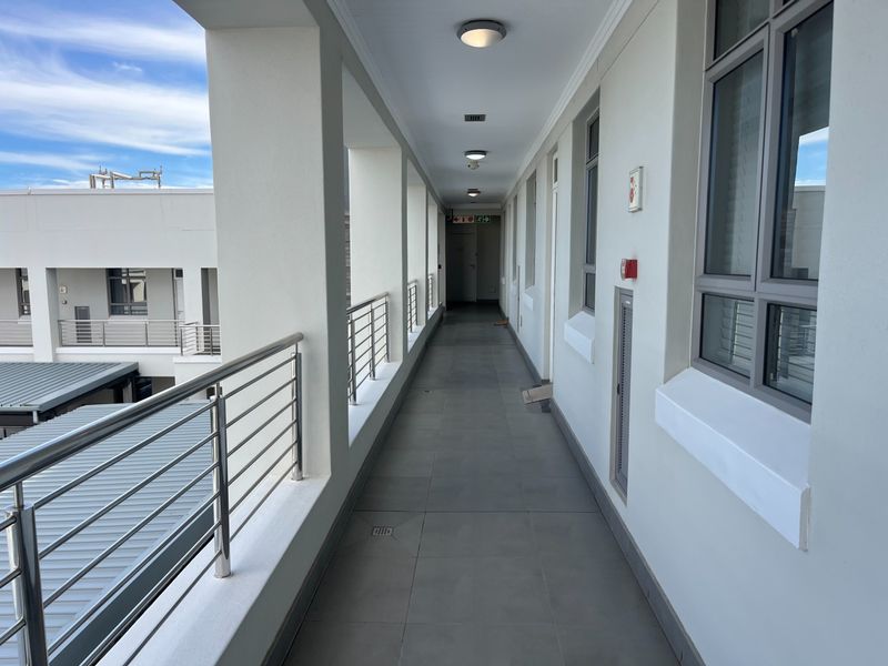A clean, well-maintained outdoor corridor featuring tiled flooring, stainless steel balustrades, and modern recessed lighting within a retirement village complex.