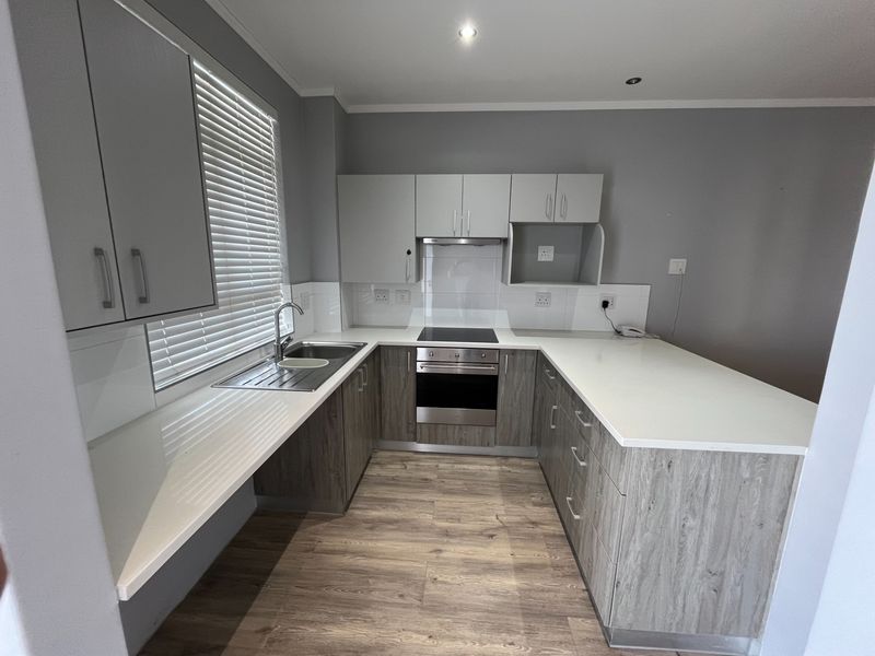 Modern kitchen featuring wood-grain cabinetry, white stone countertops, integrated electric oven and hob, and a clean tiled splashback in a neutral color palette.