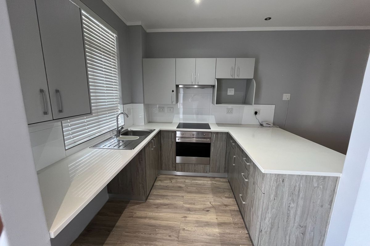 Modern kitchen featuring wood-grain cabinetry, white stone countertops, integrated electric oven and hob, and a clean tiled splashback in a neutral color palette.
