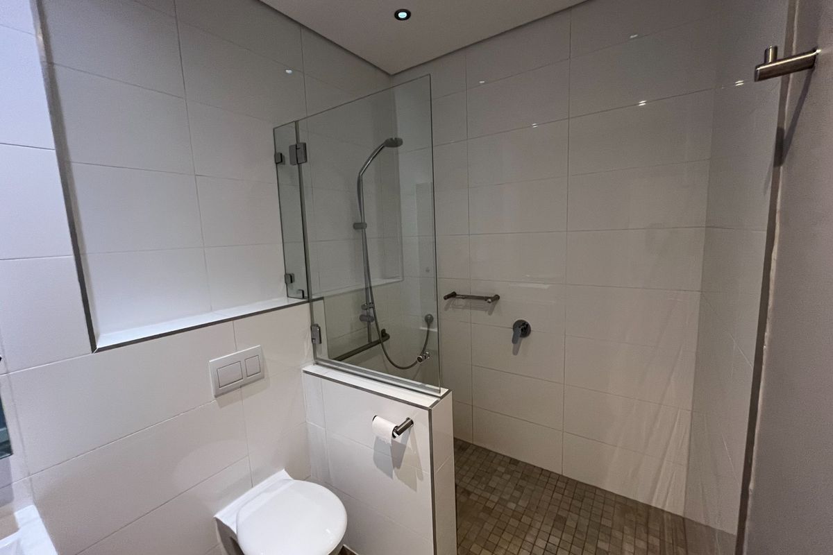 A modern, well-maintained bathroom featuring a wall-mounted toilet, a glass-enclosed shower area with mosaic tiling, and contemporary fixtures.