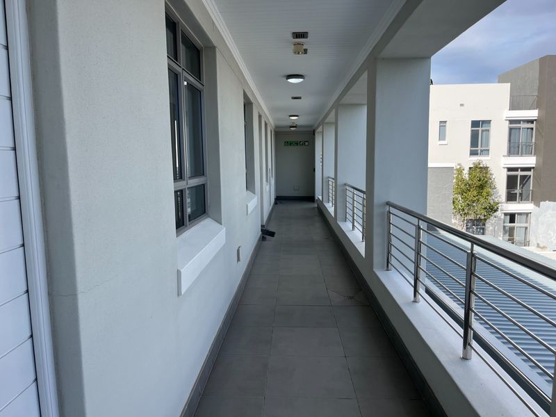 A covered outdoor walkway or balcony featuring tiled flooring, stainless steel railings, and recessed ceiling lighting, providing access to the retirement village units.