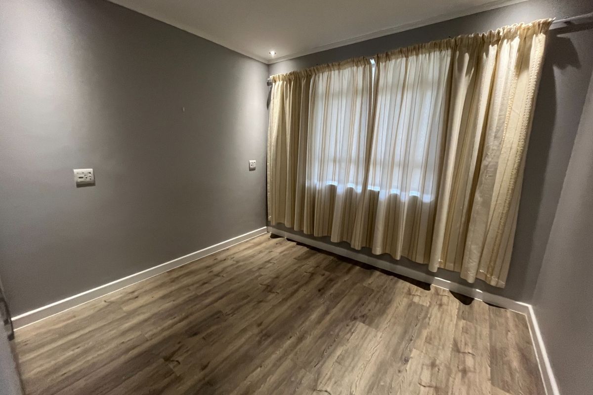 A bright, empty bedroom featuring modern laminate wood-look flooring, neutral grey walls, and recessed ceiling lighting.