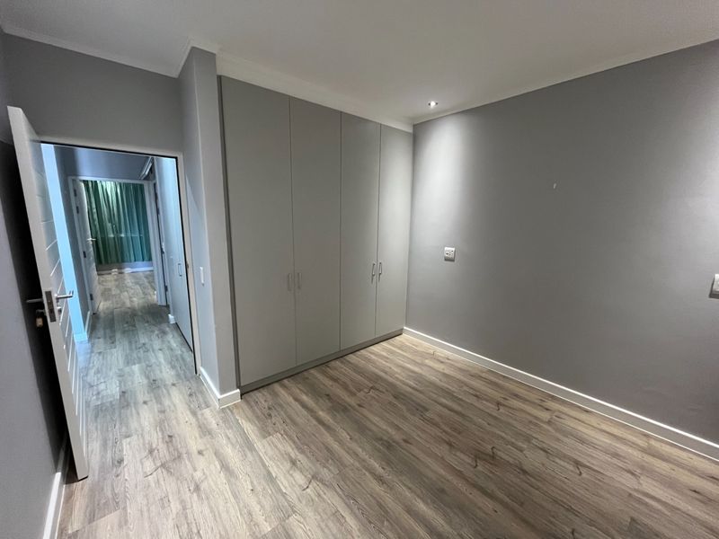 A clean, modern bedroom featuring neutral grey walls, light wood-look laminate flooring, and ample built-in cupboard storage.