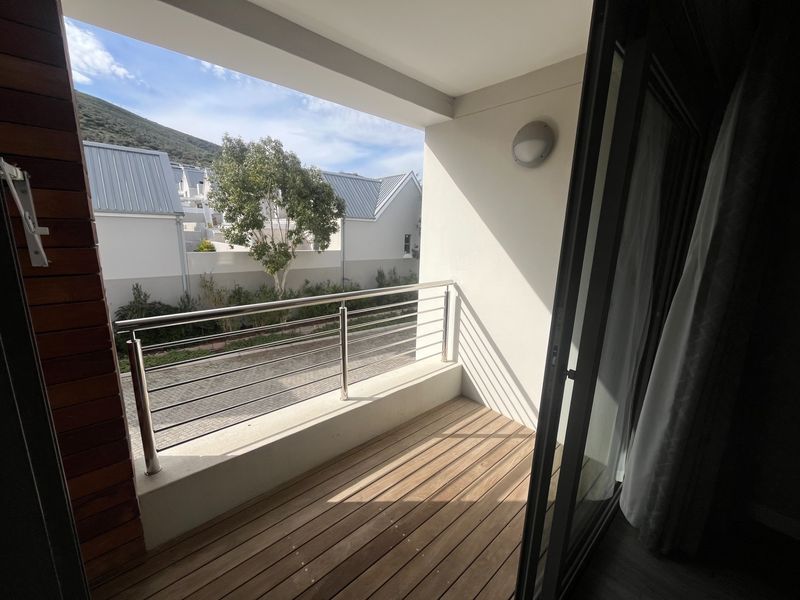 A well-maintained balcony featuring timber decking, a modern stainless steel balustrade, and a sliding glass door providing access to the outdoor space.