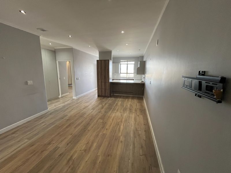Spacious open-plan living and kitchen area featuring modern laminate flooring, recessed lighting, and neutral wall finishes, providing a versatile and bright living space.