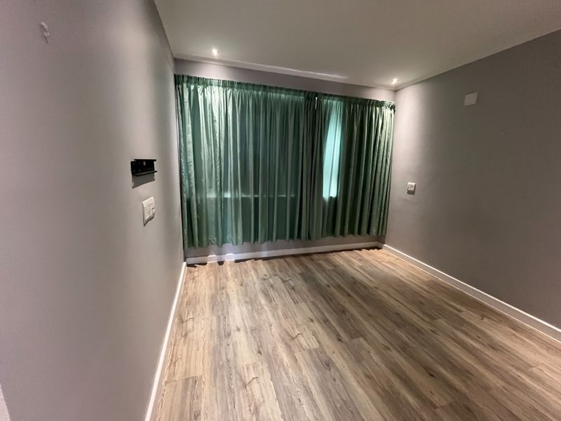 A clean, empty bedroom featuring modern laminate flooring, recessed downlights, and neutral grey walls, ready for personalization.