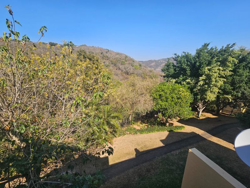 A scenic elevated view overlooking a lush garden area with mature trees and rolling hills in the background.