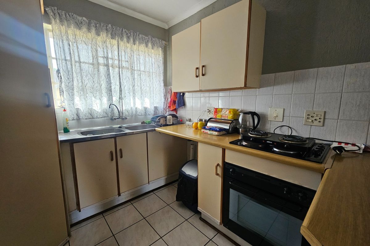 A compact, dated kitchen featuring built-in cabinetry, a double basin sink, tiled backsplash, and integrated oven and hob.