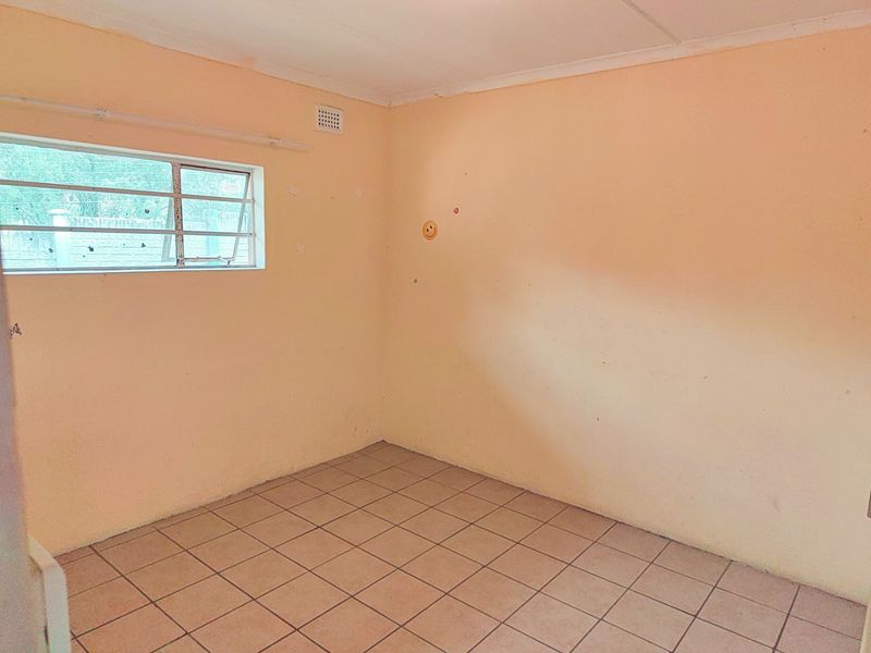 An empty bedroom featuring tiled flooring and a steel frame window, presenting a blank canvas ready for renovation or interior design updates.