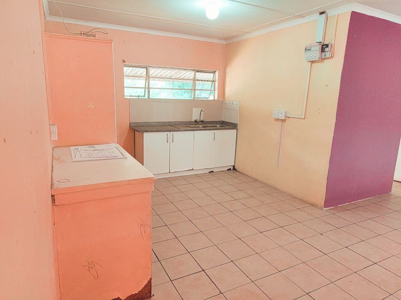 A basic, empty kitchen area featuring tiled flooring, simple cabinetry with a sink, and visible electrical infrastructure, ready for renovation or modernization.