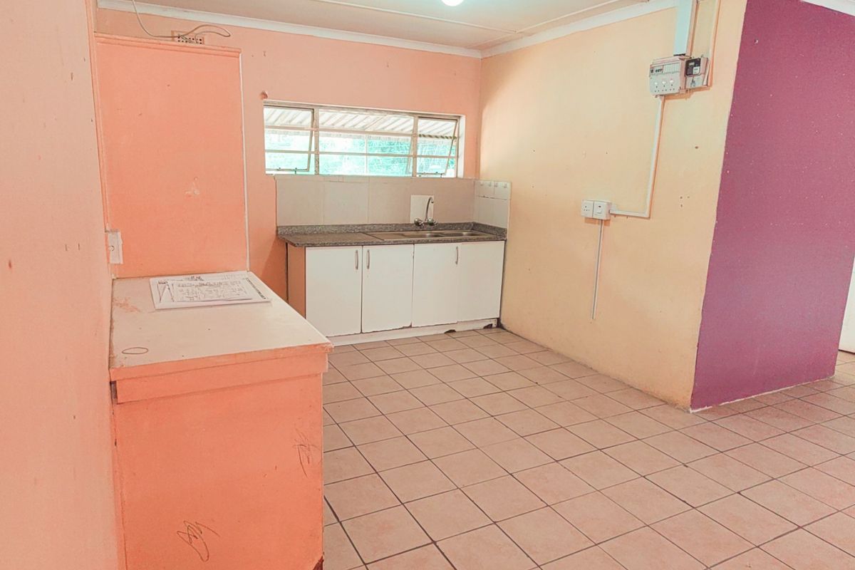 A basic, empty kitchen area featuring tiled flooring, simple cabinetry with a sink, and visible electrical infrastructure, ready for renovation or modernization.
