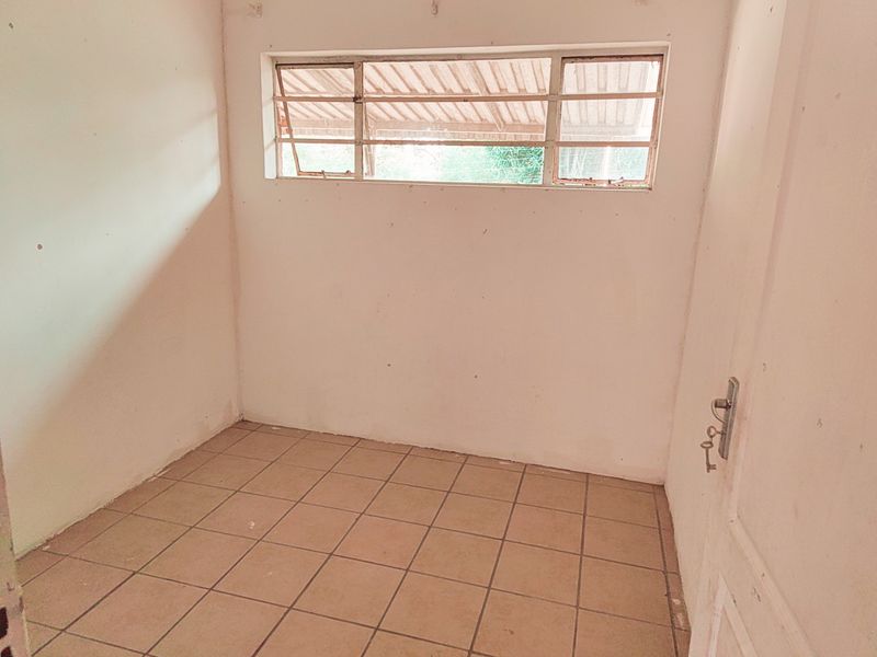 A small, empty room featuring tiled flooring and a metal-framed window, offering a blank canvas for potential renovation or bedroom use.