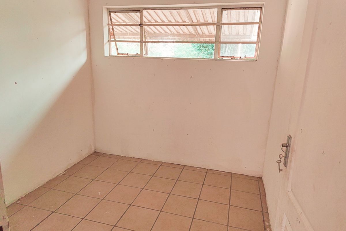 A small, empty room featuring tiled flooring and a metal-framed window, offering a blank canvas for potential renovation or bedroom use.