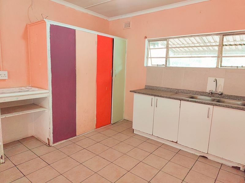 A functional kitchen space featuring tiled flooring, built-in cabinetry with a stainless steel sink, and louvered windows, offering a blank canvas for renovation.