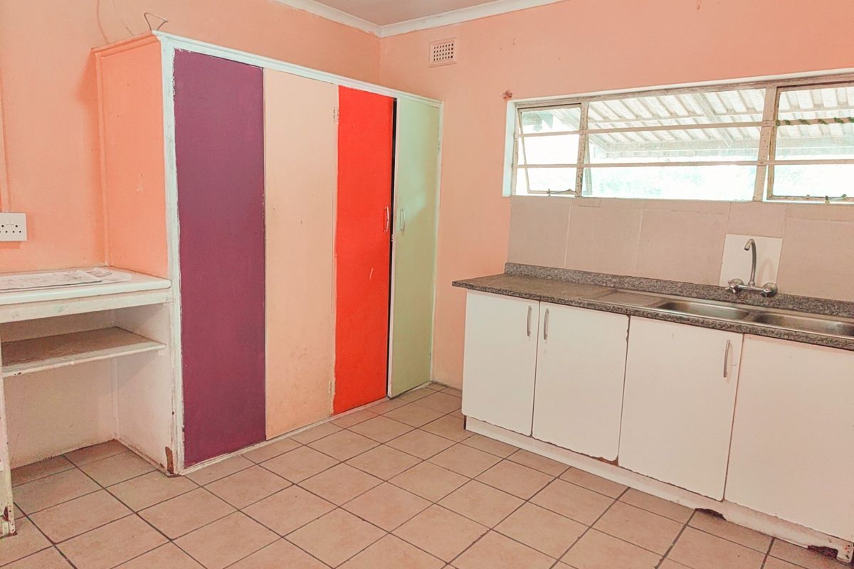 A functional kitchen space featuring tiled flooring, built-in cabinetry with a stainless steel sink, and louvered windows, offering a blank canvas for renovation.
