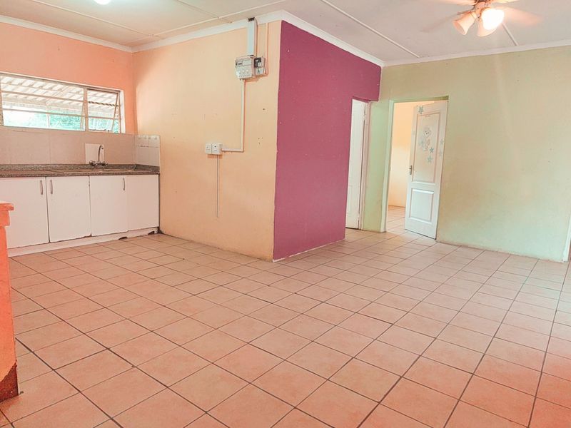 An open-plan living and kitchen area featuring tiled flooring, basic cabinetry with stone countertops, and a ceiling fan, ready for renovation or staging.