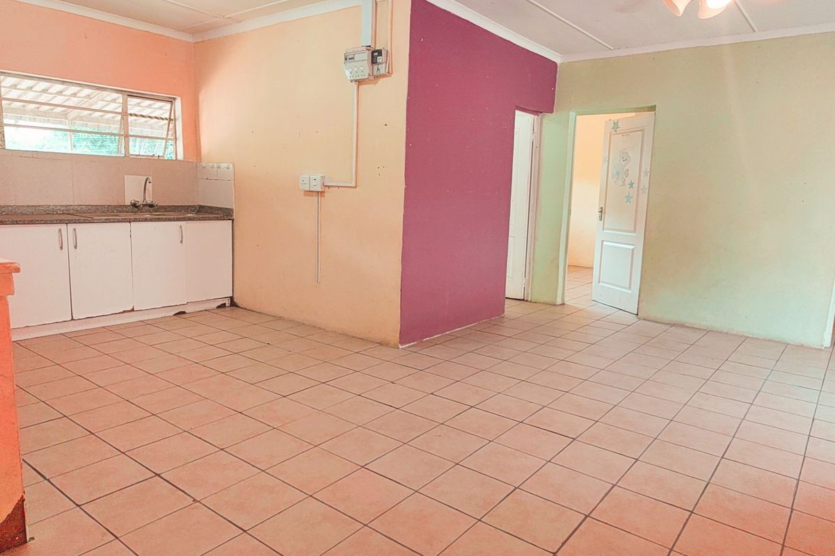 An open-plan living and kitchen area featuring tiled flooring, basic cabinetry with stone countertops, and a ceiling fan, ready for renovation or staging.