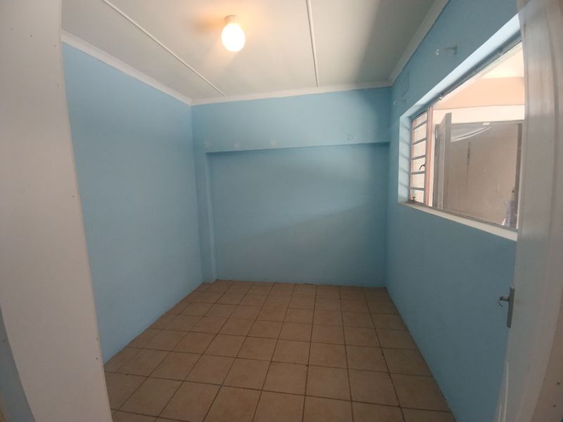An empty bedroom featuring tiled flooring, light blue walls, and an aluminium window frame, providing a blank canvas for personalization.