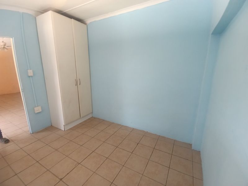 An empty bedroom featuring light blue walls, tiled flooring, and a built-in wardrobe, offering a blank canvas for personalization.