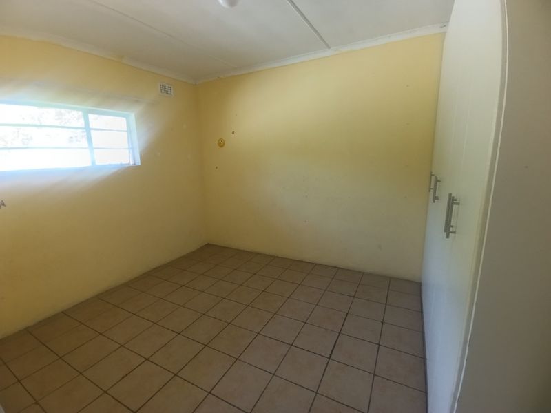 An empty bedroom featuring tiled flooring, built-in cupboards, and a window with security bars, requiring minor cosmetic updates.