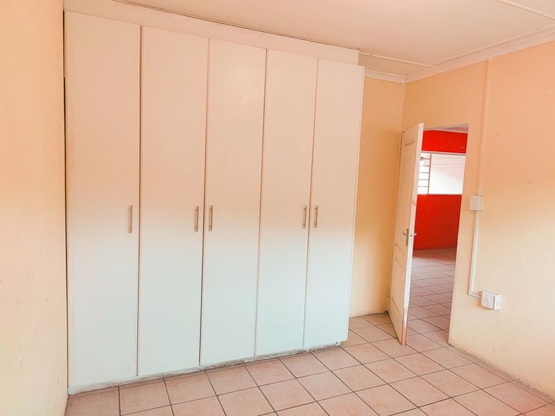 A vacant bedroom featuring built-in cupboards, tiled flooring, and an open doorway leading to an adjacent room.