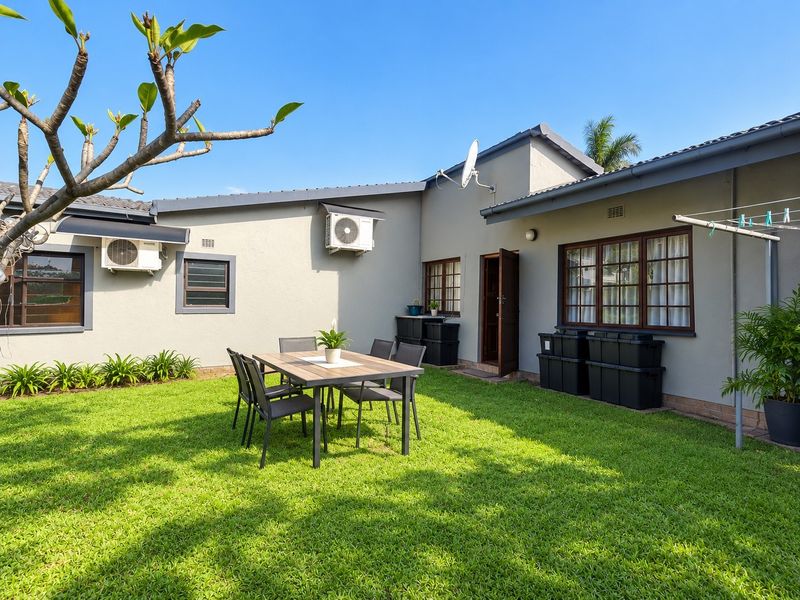 A well-maintained rear garden area featuring a lawn, exterior wall-mounted air conditioning units, and timber-framed windows.