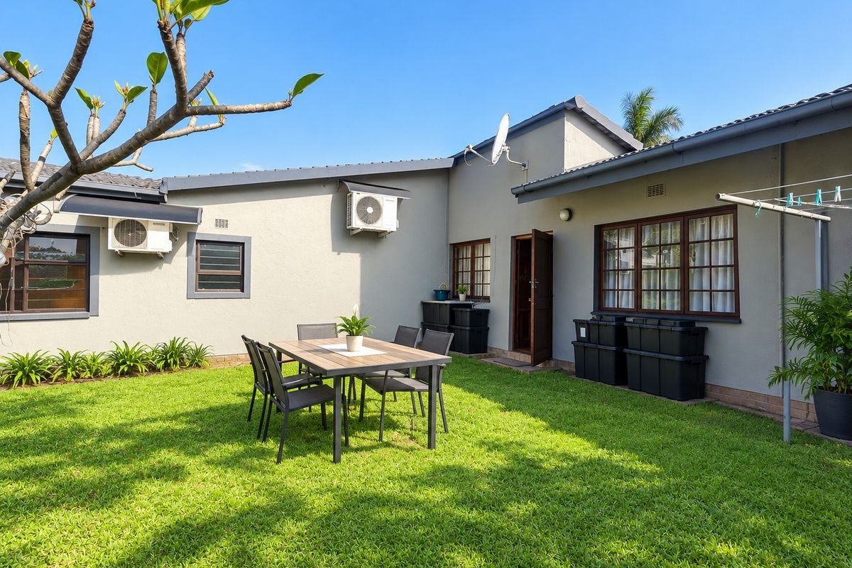 A well-maintained rear garden area featuring a lawn, exterior wall-mounted air conditioning units, and timber-framed windows.