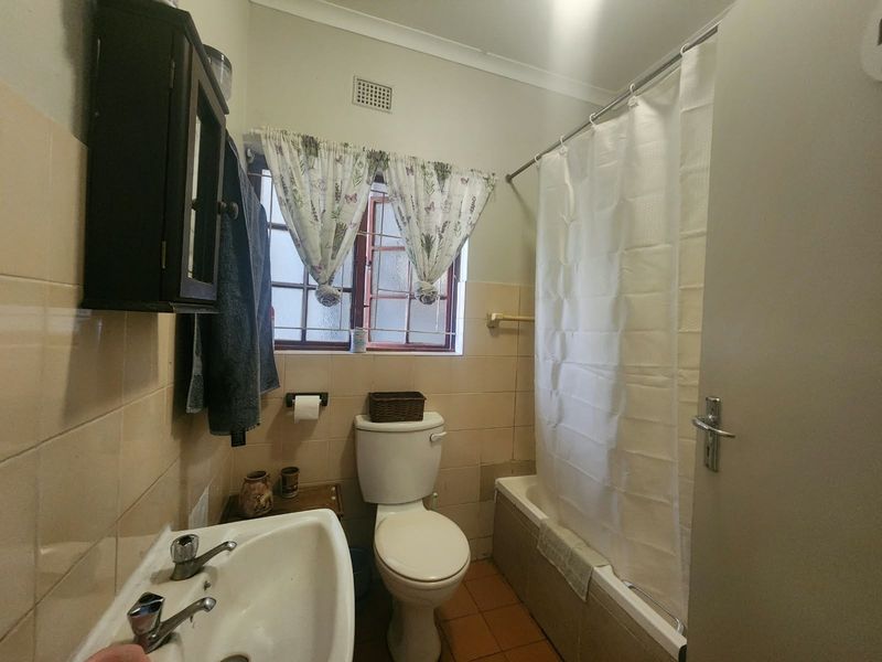 A dated bathroom featuring a bathtub with shower curtain, pedestal basin, and toilet, finished with original wall and floor tiling.
