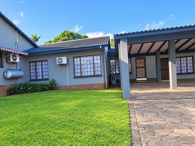A well-maintained townhouse exterior featuring a stone-paved patio, manicured lawn, brick accents, and a tiled roof with integrated air conditioning units.