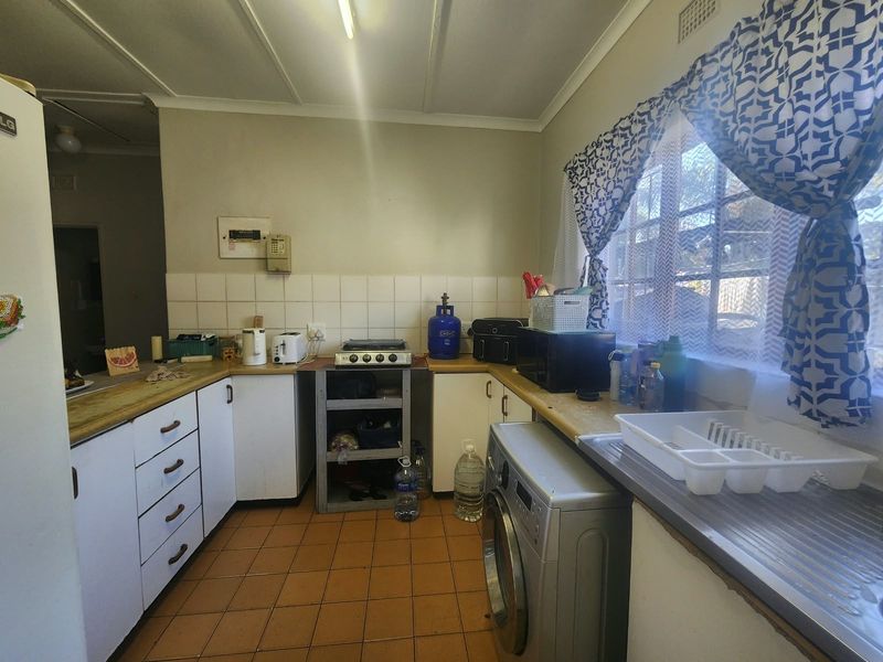 A functional kitchen featuring tiled flooring, laminate countertops, built-in cabinetry, and a gas hob, offering potential for modernization and aesthetic updates.