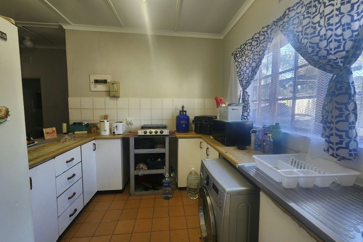 A functional kitchen featuring tiled flooring, laminate countertops, built-in cabinetry, and a gas hob, offering potential for modernization and aesthetic updates.