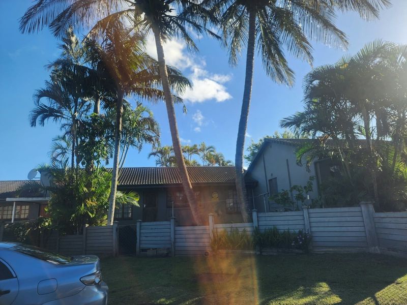 Front exterior view of the townhouse featuring a tiled roof, perimeter fencing, and established palm trees in the front garden area.