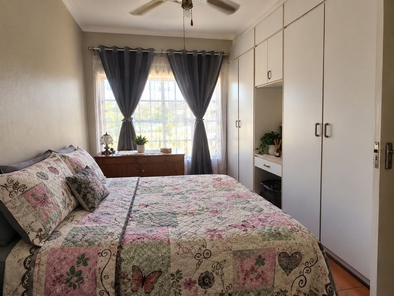 A cozy bedroom featuring built-in cupboards with an integrated vanity area, a ceiling fan, and a window fitted with security bars.