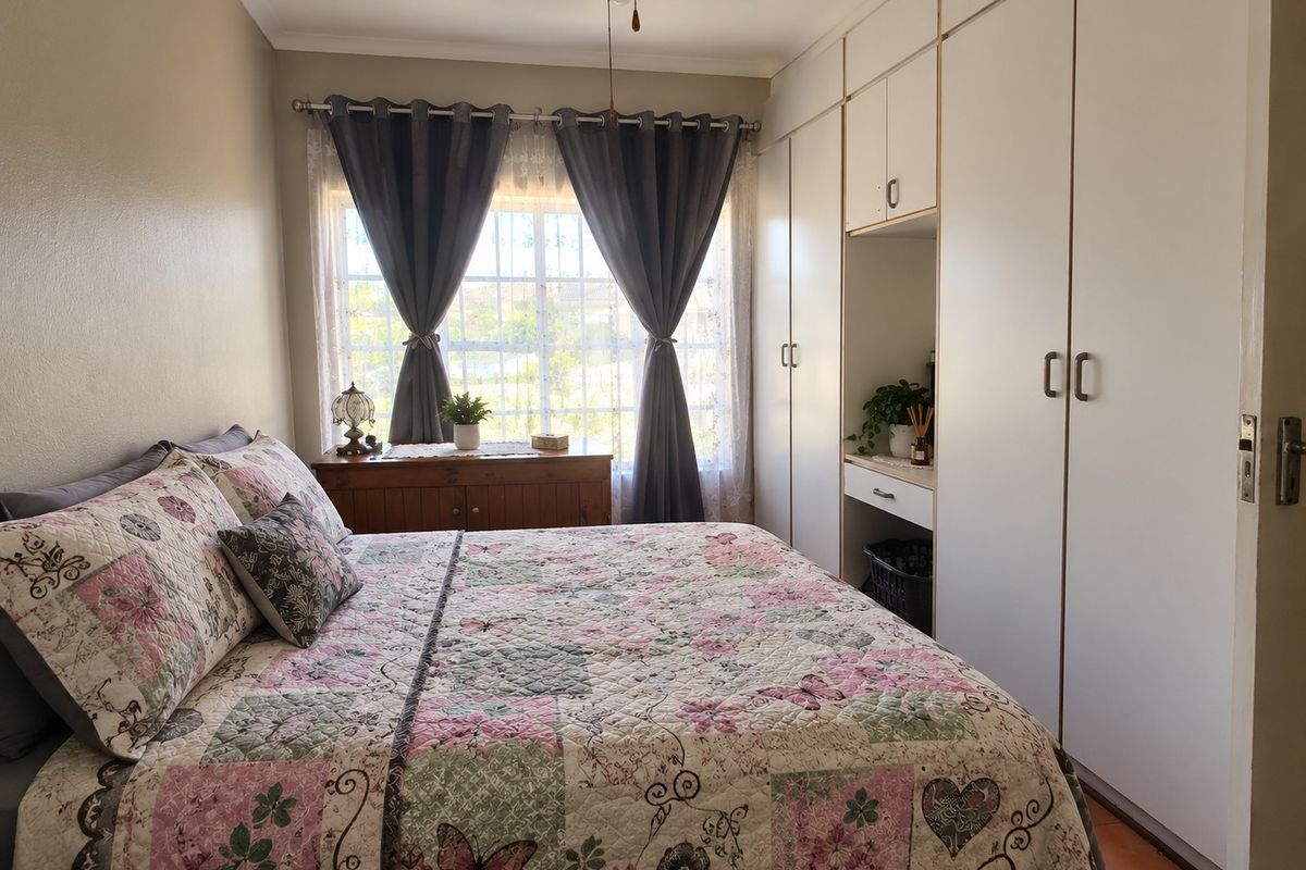 A cozy bedroom featuring built-in cupboards with an integrated vanity area, a ceiling fan, and a window fitted with security bars.