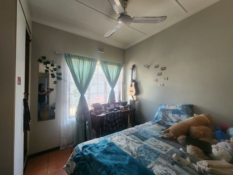 A functional bedroom featuring tiled flooring, a ceiling fan, and a built-in cupboard, offering a comfortable space with natural light.