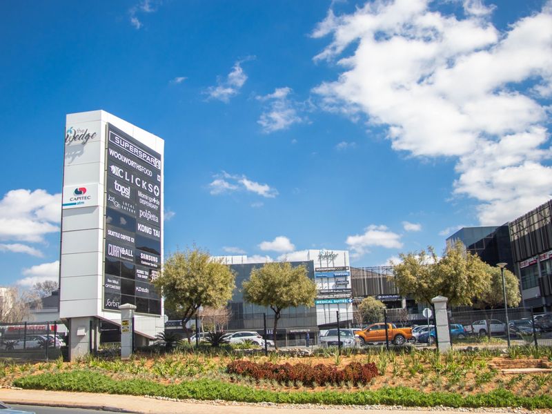 Exterior view of The Wedge commercial shopping centre featuring a prominent pylon sign, landscaped gardens, and modern building architecture.