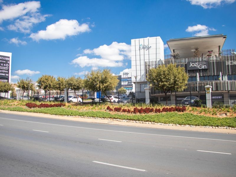 Street-level view of a modern commercial shopping center featuring prominent signage, metal facade detailing, and well-maintained landscaped verge.