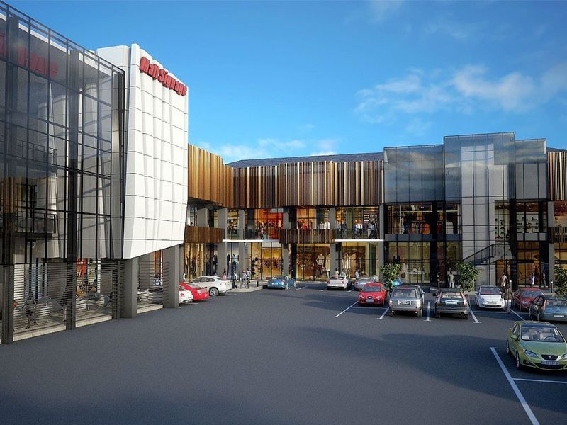 Modern commercial shopping center exterior featuring contemporary glass and metal facade design with an integrated paved parking area.