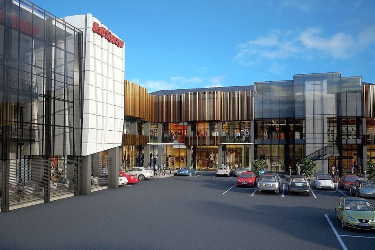 Modern commercial shopping center exterior featuring contemporary glass and metal facade design with an integrated paved parking area.