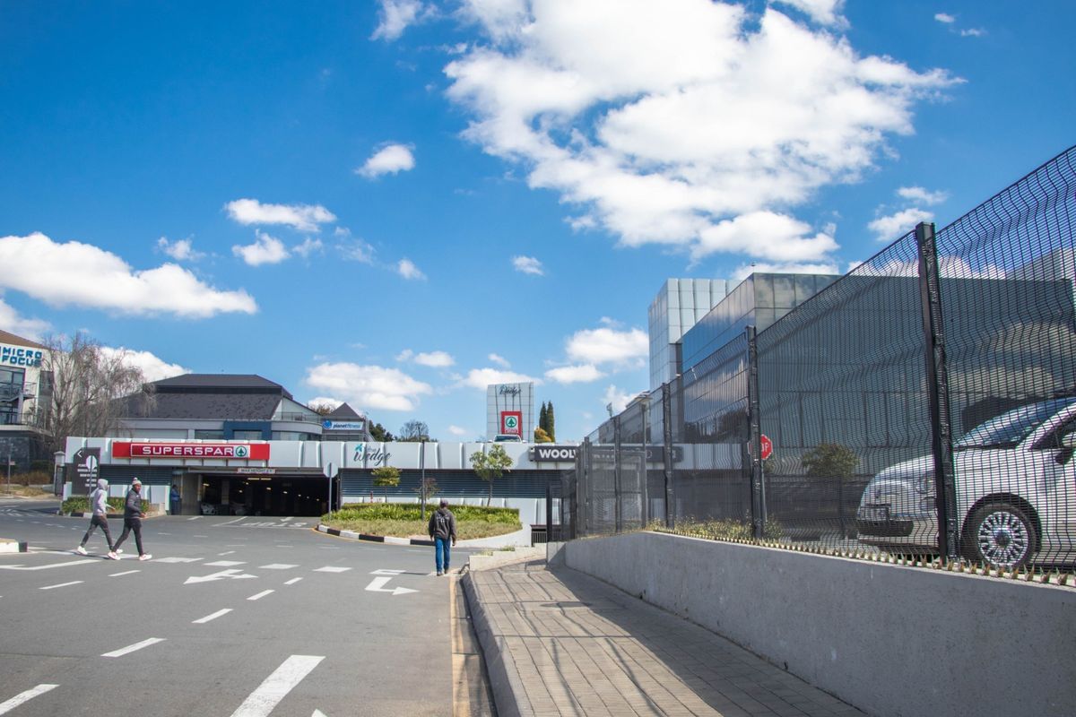 Exterior view of a commercial shopping center entrance featuring paved walkways, security fencing, and access to underground parking facilities.