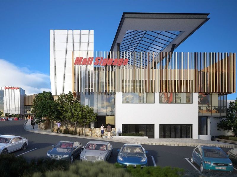 Modern commercial shopping center exterior featuring a prominent glass facade, cantilevered roof, and decorative vertical timber louvres with integrated parking.