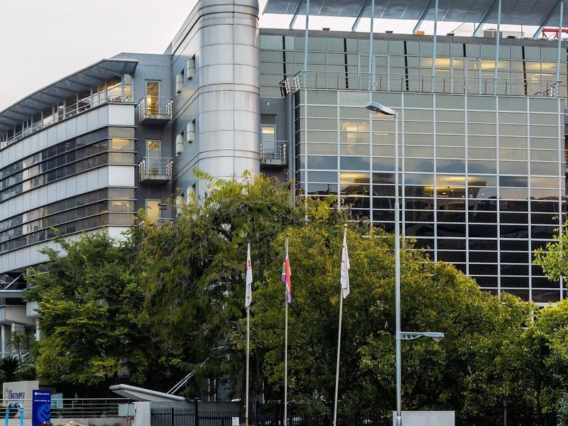 Modern commercial office building featuring a glass curtain wall facade, metal cladding, and integrated balconies, set within a landscaped environment.