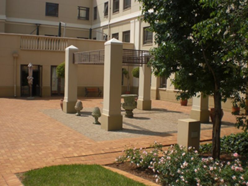 A well-maintained outdoor patio area featuring brick paving, a central pergola structure with concrete pillars, and established garden landscaping.
