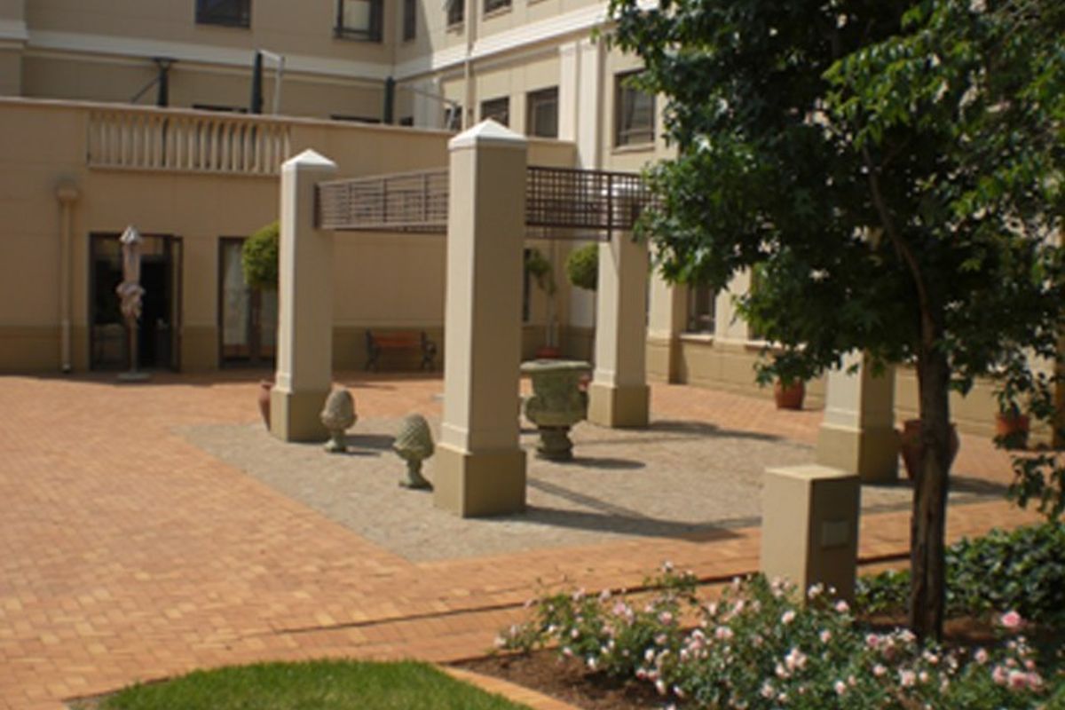 A well-maintained outdoor patio area featuring brick paving, a central pergola structure with concrete pillars, and established garden landscaping.